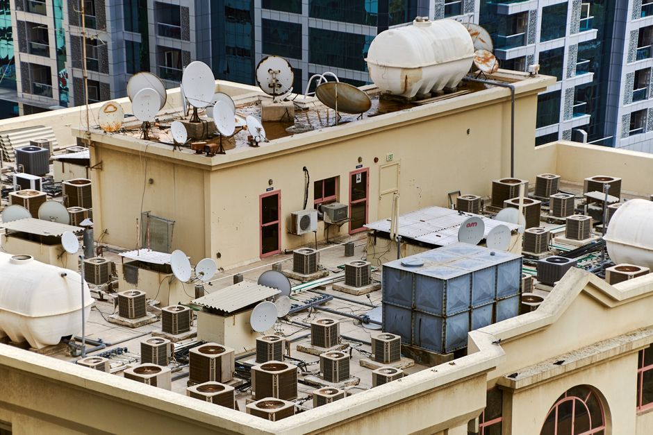 Captured from above, this urban rooftop features satellite dishes, water tanks, and HVAC units, showcasing city infrastructure.
